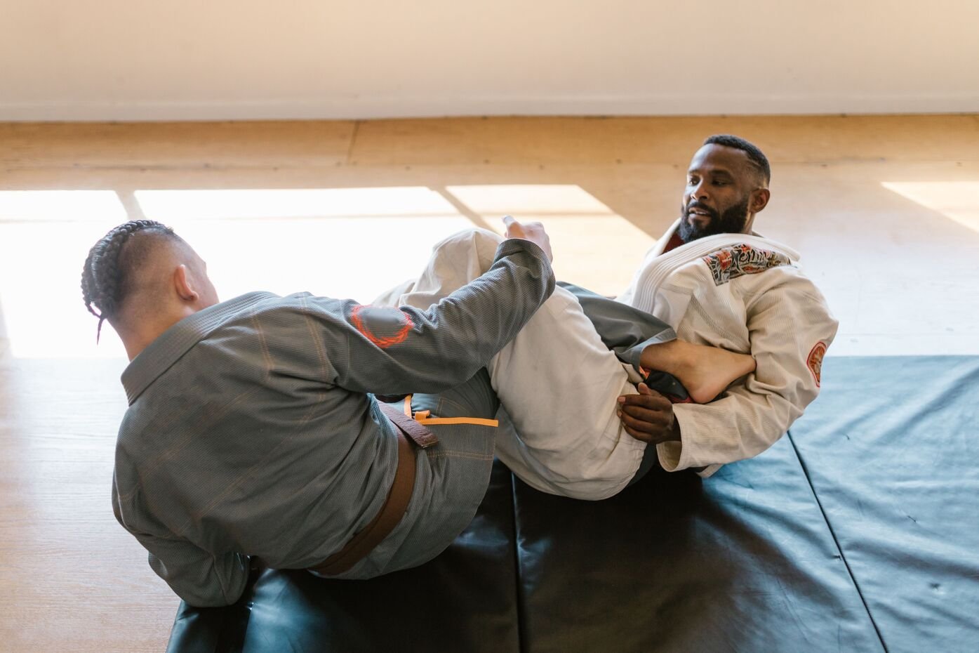 Dos practicantes de jiujitsu brasileño haciendo demostración de lucha en el piso vistiendo sus kimonos.