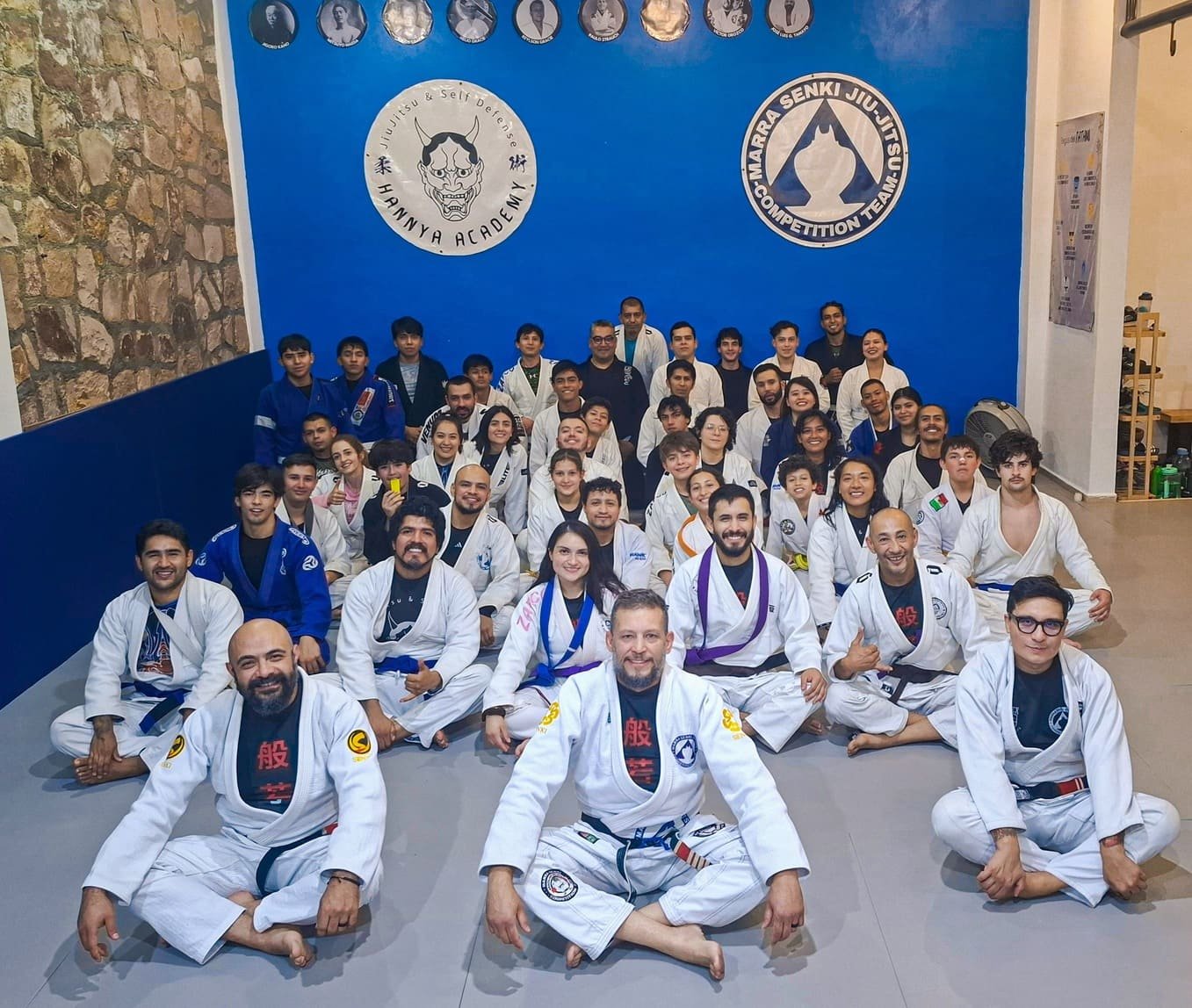 Comunidad Hannya Academy guanajuato portando sus gi tradicionales color blanco sentados en el tatami con sus logos de fondo